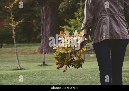 Donna in piedi in un giardino che tiene rami con foglie d'autunno Foto Stock