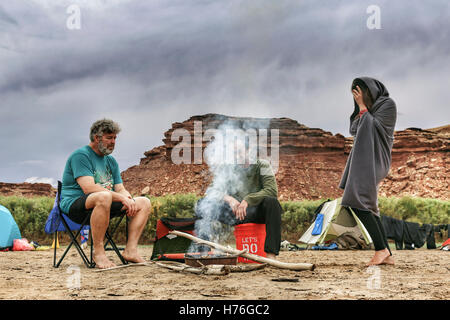 Una famiglia di naviganti si siede e si erge attorno a un fuoco di driftwood dopo una pioggia sul fiume verde nel Parco Nazionale di Canyonlands, Foto Stock