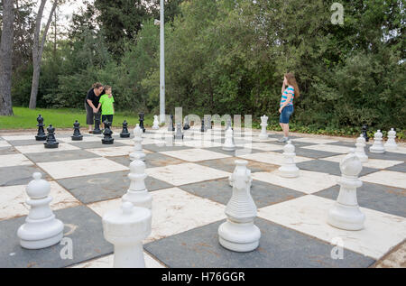 Fratello, sorella e madre giocando a un gioco di gigante scacchi all'aperto con pezzi di grandi dimensioni in un verde parco all'aperto Foto Stock