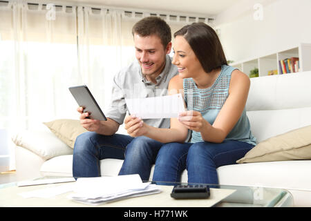 Felice coppia controllo conto bancario on line in una compressa seduta su un divano nel salotto di casa Foto Stock