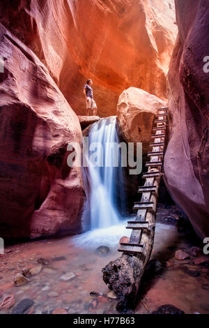 Donna che si erge sopra la cascata, canyon rosso slot, Utah, Stati Uniti Foto Stock