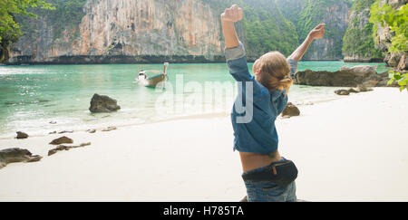 Vista posteriore del turista femminile in blue jeans maglietta e pantaloni corti permanente sulla spiaggia con le mani alzate e godendo di estate su Foto Stock