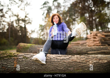 Senior runner seduti su tronchi di legno, stretching, acqua potabile Foto Stock