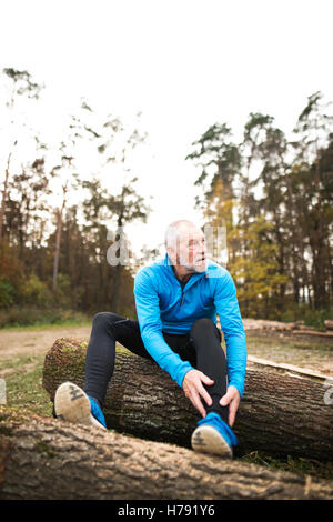 Senior runner seduti su tronchi di legno, uomo appoggiato, stretching. Foto Stock