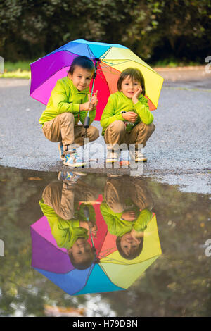 Due adorabili poco ragazzi con ombrello in un parco in un giorno di pioggia, giocando e saltando, sorridente, parlare insieme, autumntime Foto Stock