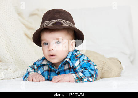 Baby ritratto giacciono su asciugamano bianco nel letto, vestito di plaid shirt e hat Foto Stock