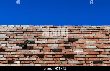 Il vecchio muro di mattoni contro il cielo luminoso Foto Stock