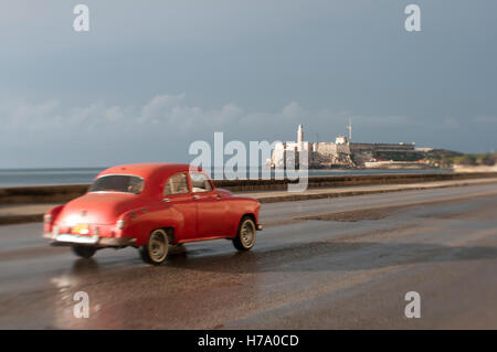 Trasognata tilt-shift vista panoramica di vintage americano auto taxi guida nella parte anteriore di el Morro faro lungo il Malecon a l'Avana Foto Stock