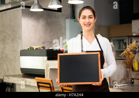 Bella donna caucasica nel grembiule barista azienda lavagna vuota segno dentro coffee shop - pronti per inserire il testo Foto Stock