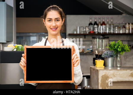 Bella donna caucasica nel grembiule barista azienda lavagna vuota segno dentro coffee shop - pronti per inserire il testo Foto Stock