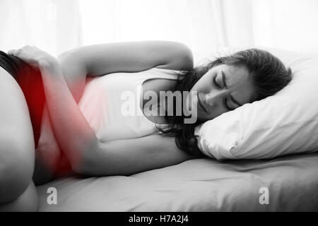 Giovane bella donna caucasica su letto di dolore allo stomaco / periodo le mestruazioni / avvelenamento alimentare / crampi malattia (nero e W Foto Stock