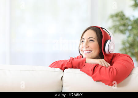 Dreamer girl teen ascolto di musica con cuffie su un divano nel soggiorno di casa e guardando al di sopra con lo spazio di copia Foto Stock