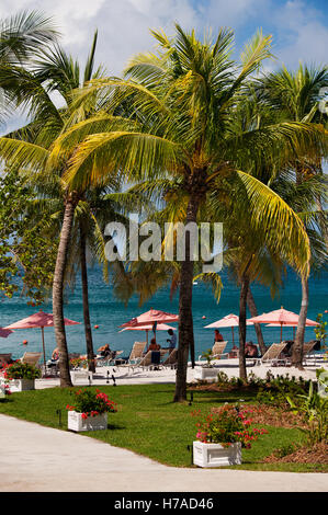 Le persone a rilassarsi sotto sbiadito ombrelloni in spiaggia appartata resort sull'isola caraibica di Saint Lucia Foto Stock