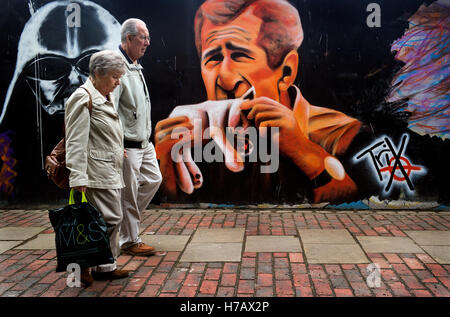 Street graffiti che mostra una somiglianza dell ex Presidente degli Stati Uniti George Bush di mordere in un gatto come 2 persone a piedi passato. Foto Stock