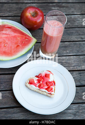 A forma di cuore ad toast con formaggio bianco, anguria e strawerry sirpo. Una mela rossa anguria e frutta e succhi di frutta. Red halthy bre Foto Stock