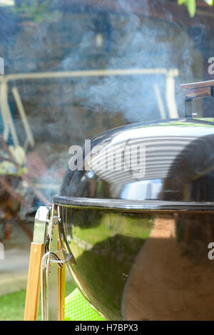 Il fumo uscire da un barbecue chiuso durante la tirata grigliate di carne di maiale Foto Stock