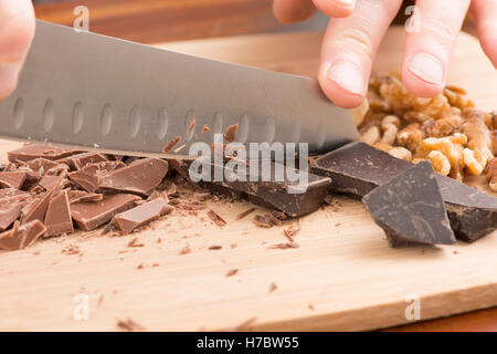 Chef cioccolato tritare con il coltello sul tagliere. Preparazione di dessert in cucina con luce e cioccolato fondente. Foto Stock