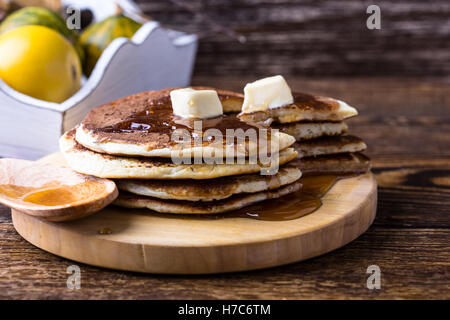 Frittelle fatte in casa servite calde con burro e sciroppo d'acero su tavola in legno rustico Foto Stock