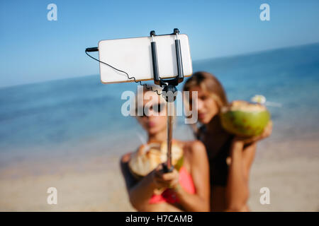 Due giovani amici di sesso femminile prendendo autoritratto con lo smartphone sulla spiaggia. Le donne in vacanza sulla spiaggia prendendo selfie. Focus su mobil Foto Stock