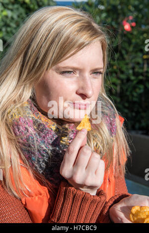 Attraente donna bionda mangiare patatine da mano Foto Stock