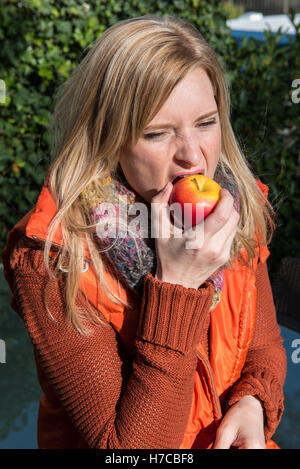 Attraente donna bionda di mordere in un Apple Foto Stock