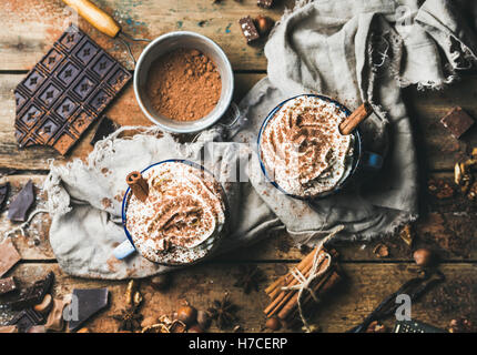 Cioccolata calda con panna montata e bastoncini di cannella servita con anice, dadi e cacao in polvere di legno rustico sfondo, top v Foto Stock