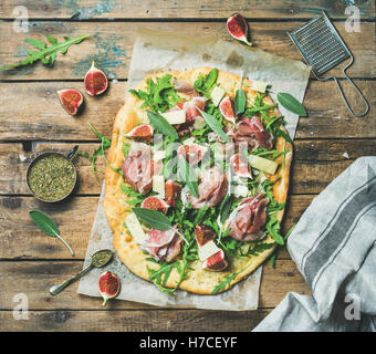 Fig, prosciutto, rucola e salvia flatbread pizza con le spezie in tazza sulla carta da forno su legno rustico sfondo, vista dall'alto Foto Stock