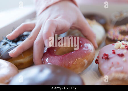 A mano selezionando una ciambella da una scatola di una dozzina di ciambelle. Foto Stock