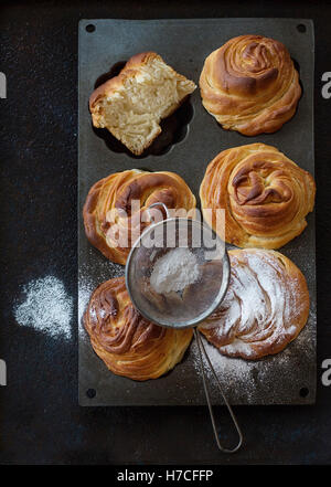 Freschi di forno pasticceria moderna cruffins, come croissant e muffin con lo zucchero in polvere, servita in silicio forma di cottura con setaccio oltre Foto Stock