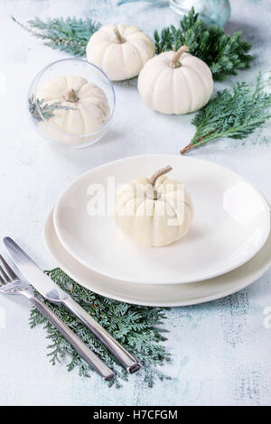 Holiday messa in tavola decorazione bianco con zucche decorative, thuja filiali e la cena piatti su bianco sullo sfondo di legno. Foto Stock