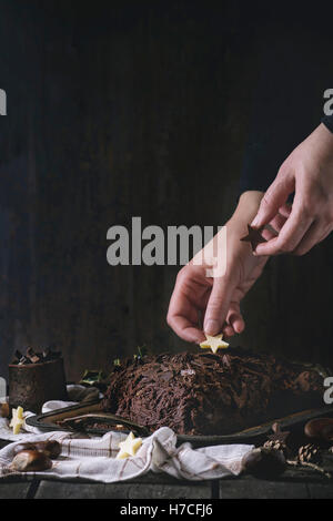 Processo di decorazione di Natale fatti in casa il cioccolato yule log da donna con le mani il cioccolato stelle sopra il vecchio tavolo in legno con hol Foto Stock