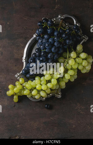 I grappoli di ripe rosso bagnato e uve bianche su vintage vassoio metallico sopra il vecchio legno scuro dello sfondo. Vista da sopra con spazio per il testo. Da Foto Stock