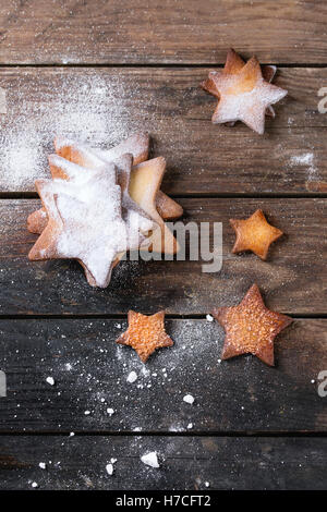 In casa frollini forma a stella i cookie di zucchero di diverse dimensioni con polvere di zucchero scuro sulla superficie di legno. Dolcetti di Natale backgroun Foto Stock