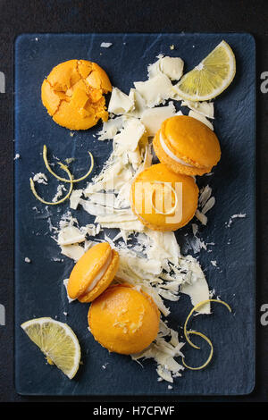 Tutto rotto e arancione in casa limone amaretti con cioccolato bianco tritato e citrus lo zucchero e la scorza in vetro scuro su scheda Foto Stock