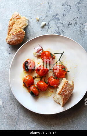 Arrosto di pomodoro ciliegino con olio di oliva e sale marino su una piastra bianca.vista superiore Foto Stock