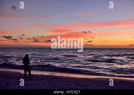 Donna sulla spiaggia di sabbia vicino a silhouette con il mare di fronte Foto Stock