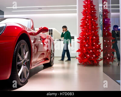 SHOWROOM AUTO DI NATALE Red Ferrari 'California' in mostra In vendita in showroom con albero di Natale rosso e giovane ragazzo al telefono dietro Foto Stock