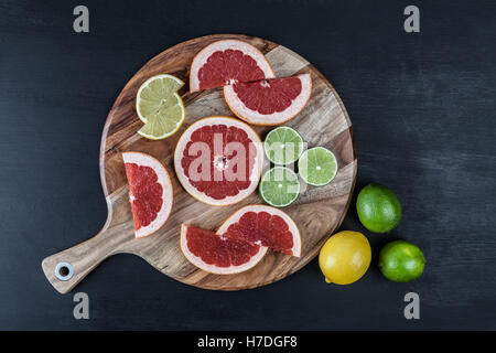 Fette di agrumi sul round tagliere con tutto il limone e lime. Vista da sopra con lo spazio di copia Foto Stock