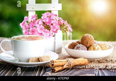 Tazza di caffè, fiori e dolci shekoladnye su un vecchio tavolo in legno Foto Stock