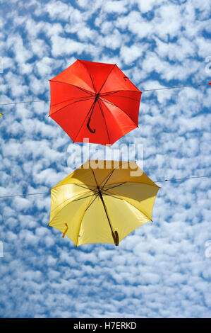 Ombrelli dai colori vivaci contro un cielo puntellato di nuvole, decorando una strada commerciale a Barcelos, Portogallo Foto Stock