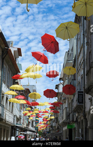 Ombrelli dai colori vivaci contro un cielo puntellato di nuvole, decorando una strada commerciale a Barcelos, Portogallo Foto Stock