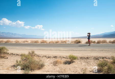 Giovane uomo in piedi sulla strada, fotografare, Highway 190, il Parco Nazionale della Valle della Morte, CALIFORNIA, STATI UNITI D'AMERICA Foto Stock