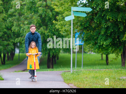 Poco adorabili ragazze a cavallo su scooter con papà in autunno parcheggiare all'esterno Foto Stock