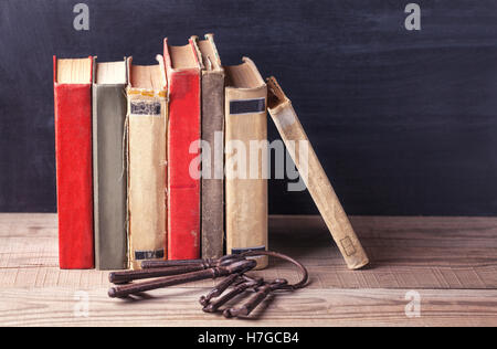 Pila di vecchi libri vintage e un mucchio di grandi chiavi di ferro giacciono su di un tavolo di legno. Foto Stock