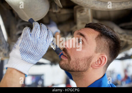 Uomo meccanico con torcia a riparazione auto in negozio Foto Stock