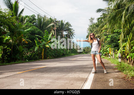 Giovane donna autostop lungo una strada Foto Stock