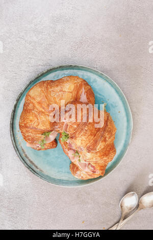 Brioche per la prima colazione. Due cornetti ripieni di formaggio, prosciutto e pancetta affumicata su sfondo grigio. Vista dall'alto, uno spazio vuoto,stile retrò Foto Stock