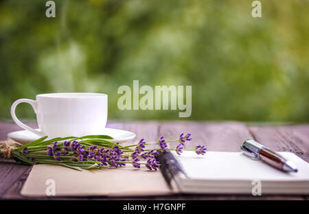 Vuoto notebook bianco, fiori e la tazza di caffè sulla scrivania all'aperto in estate Foto Stock