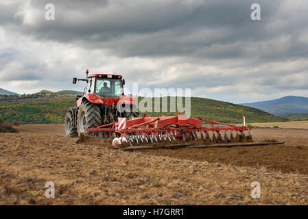 L'agricoltore nel trattore la preparazione di terra con il coltivatore del letto di semina Foto Stock