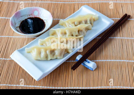 Gyoza potstickers o su una piastra su un tappetino di bambù, con bacchette e salsa di immersione. Foto Stock